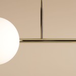 Złota lampa sufitowa Dione z czterema punktami świetlnymi. Konstrukcja metalowa, z białymi kulistymi kloszami, zawieszona na poziomej belce. Ujęcie z bliska, ukazujące detale wykończenia i kształt kloszy. Tło w delikatnym beżu.