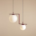 Lampa wisząca Zac II 2-punktowa w kolorze czerwonym, z dwiema białymi kulami szklanymi. Zawieszona na cienkich czarnych przewodach, z geometrycznym metalowym stelażem. Górna kula większa, dolna mniejsza, układ asymetryczny. Tło jasne, jednolite.