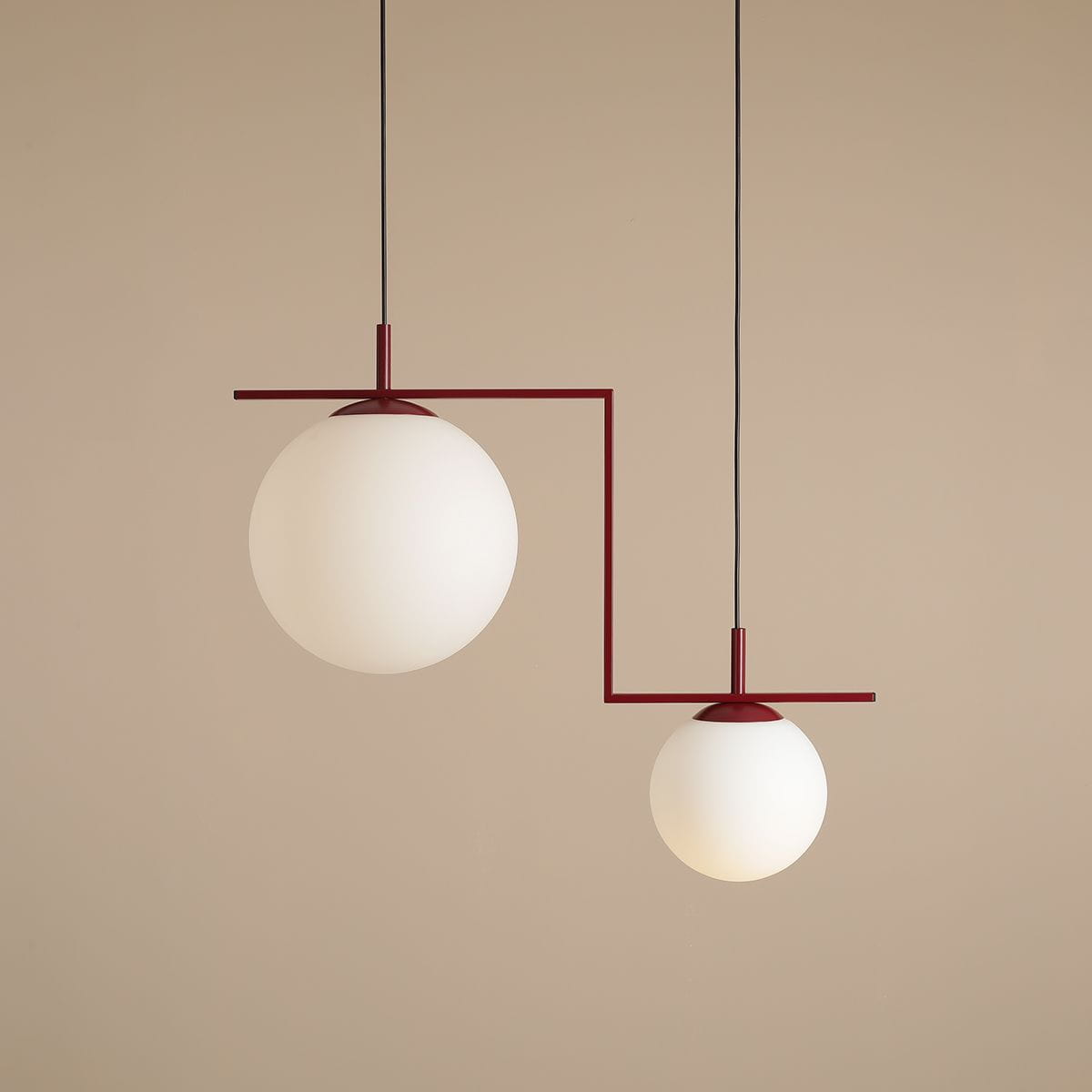 Lampa wisząca Zac II 2-punktowa w kolorze czerwonym z dwiema okrągłymi kloszami z matowego szkła. Ułożona w asymetryczny sposób, z większym kloszem zawieszonym wyżej i mniejszym niżej, na prostym, czerwonym stelażu. Tło w jasnym odcieniu beżu.