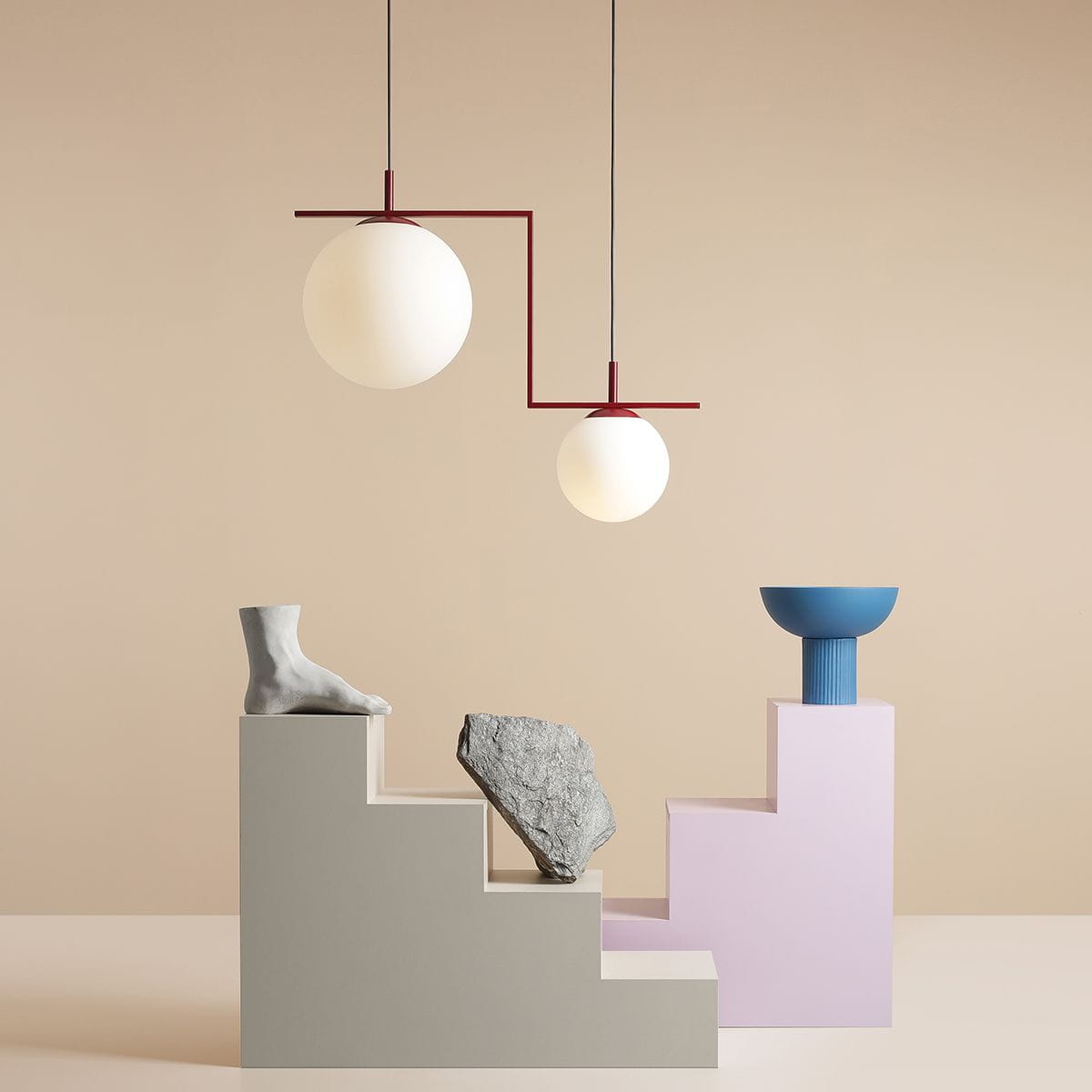 Zac II to czerwona lampa wisząca z dwoma okrągłymi kloszami w białym kolorze. Ujęcie z boku, lampa zawieszona na cienkich linkach, w tle minimalistyczna aranżacja z geometrycznymi elementami. Idealna do nowoczesnych wnętrz.