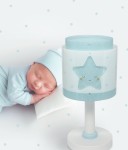 Lampka nocna w kształcie gwiazdki w pastelowym niebieskim kolorze, z uśmiechniętą buźką i białym podstawnikiem. Produkt stoi na stole obok śpiącego niemowlęcia, w tle delikatne kropki na ścianie.