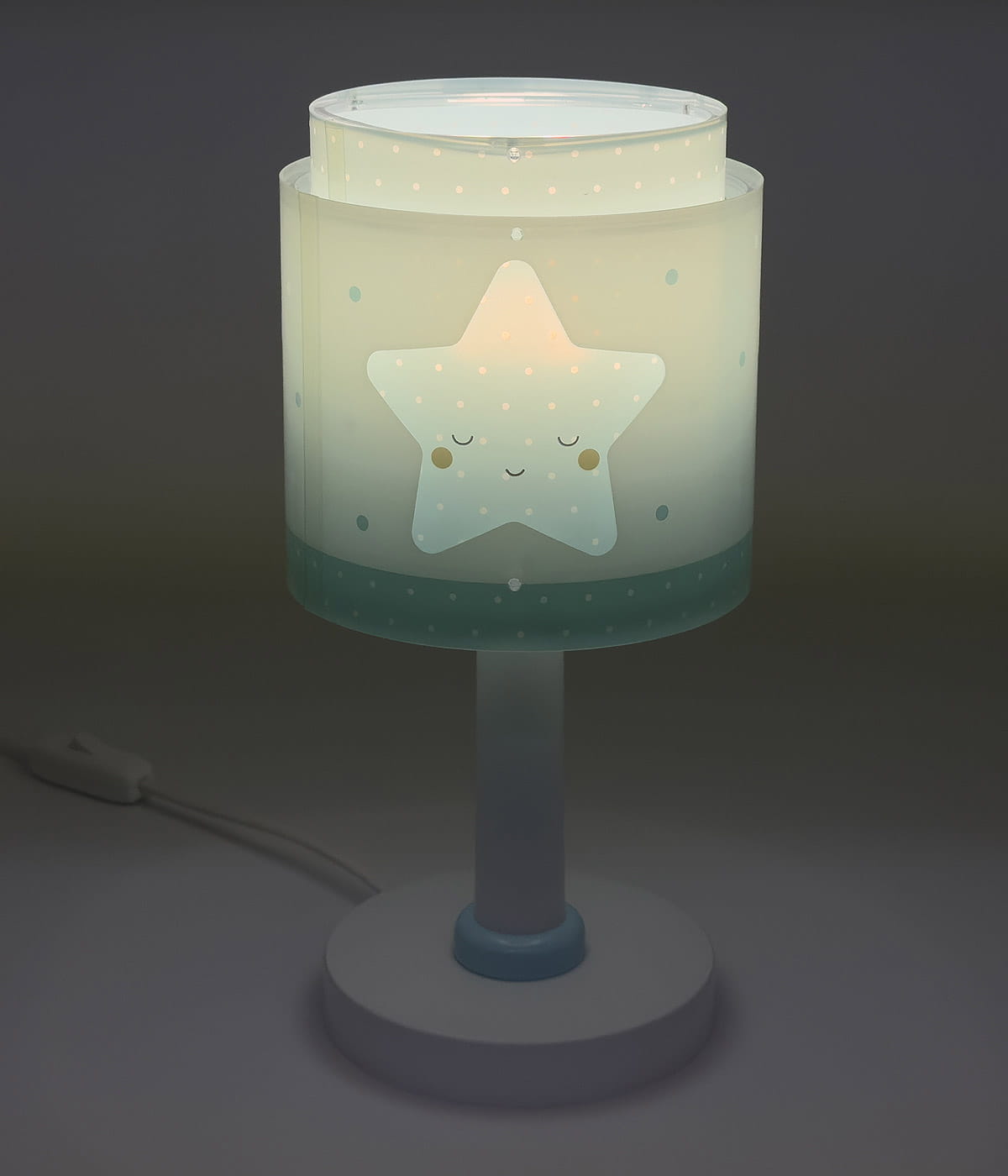 Lampka nocna 1-punktowa w kształcie gwiazdki, z przezroczystym kloszem w kolorze jasnym, ozdobionym białymi kropkami i uśmiechniętą gwiazdką. Stojąca na okrągłej, białej podstawie z niebieskim akcentem. Kabel zasilający widoczny z boku.
