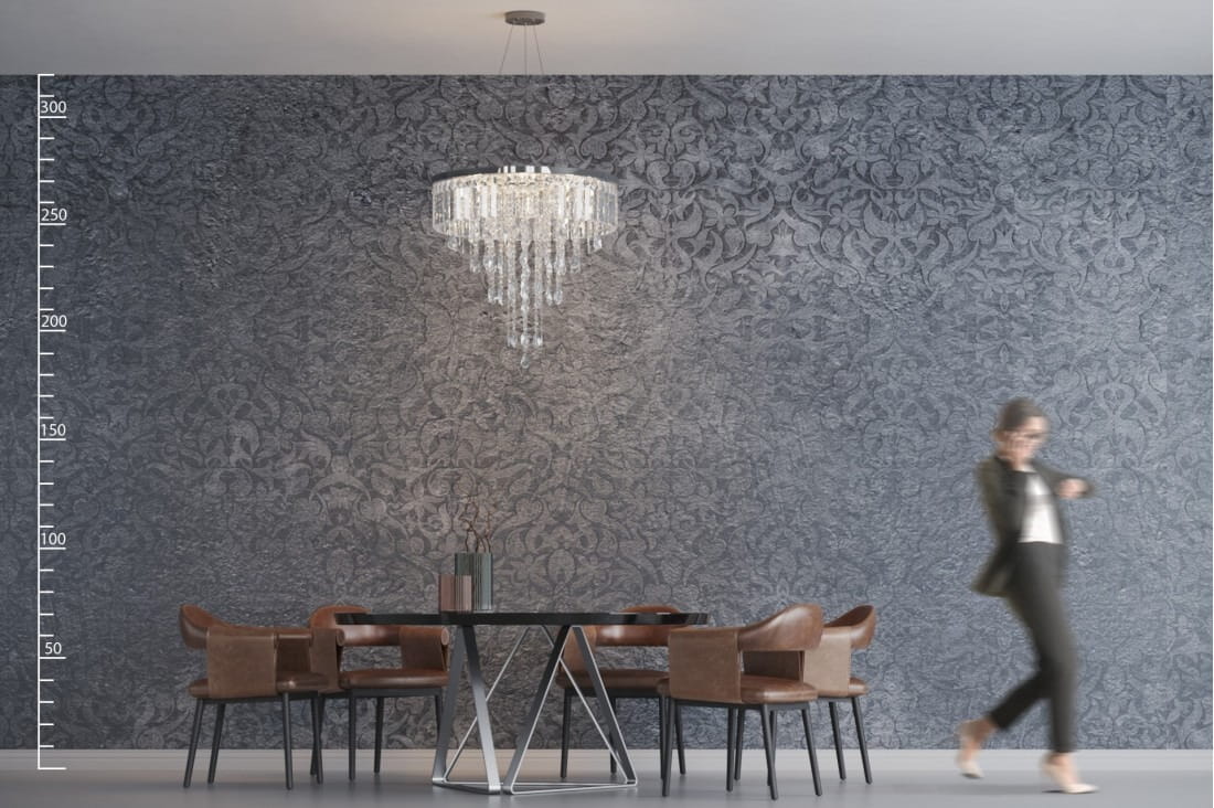Lampa wisząca Kalabria XL 12-punktowa w złotym kolorze, z kryształowymi detalami, zawieszona na cienkim przewodzie. Ujęcie frontalne, lampa umieszczona nad okrągłym stołem z czarnym blatem i brązowymi krzesłami, w tle elegancka, wzorzysta ściana.