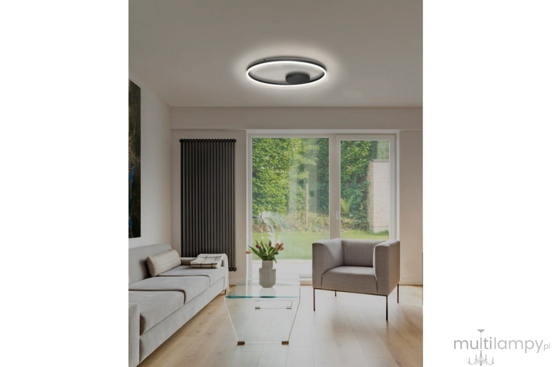 Czarna lampa sufitowa Halo D60 LED o okrągłym kształcie, zamontowana na suficie. Emituje miękkie światło, otoczona jest przez cienką, białą ramkę. Lampa znajduje się w nowoczesnym wnętrzu z sofą, stolikiem i oknami.
