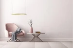 Złota lampa wisząca Halo D80 LED, umieszczona nad stołem, w minimalistycznym wnętrzu. Lampa ma okrągły kształt, zawieszona na cienkich linkach. W tle widoczny różowy fotel z szarym kocem oraz różowa wazon z gałązką. Ściana ma jasny, gładki kolor.
