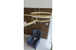 Lampa wisząca Halo 100+80+60 LED w kolorze złotym, składająca się z trzech okrągłych pierścieni, zawieszona na cienkich linkach. Ujęcie z góry, w tle widoczny niebieski fotel na tle drewnianej, poziomej ścianki.