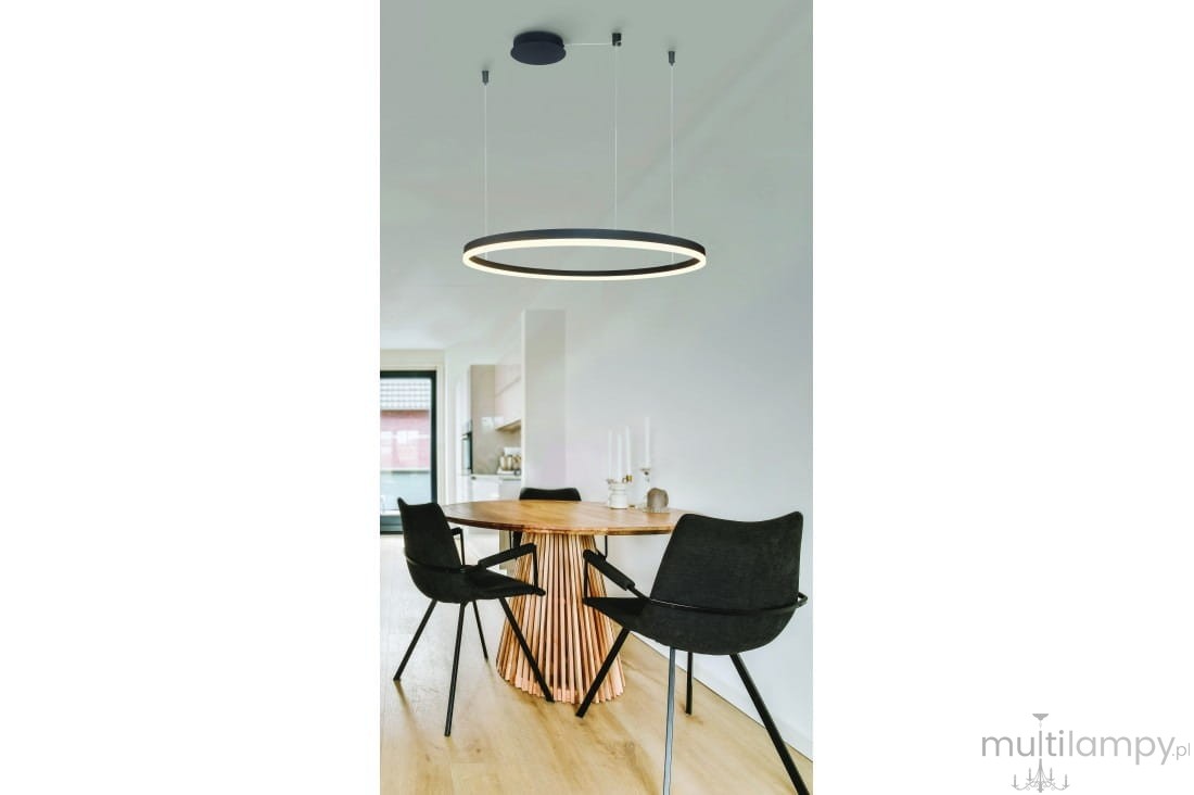 Czarna lampa wisząca Halo D150 LED z pilotem, w formie okrągłego pierścienia, zawieszona na cienkich linkach. Lampa znajduje się nad okrągłym stołem z drewnianym blatem i czarnymi krzesłami w nowoczesnym wnętrzu.
