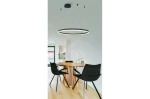 Czarna lampa wisząca Halo D150 LED z pilotem, w formie okrągłego pierścienia, zawieszona na cienkich linkach. Lampa znajduje się nad okrągłym stołem z drewnianym blatem i czarnymi krzesłami w nowoczesnym wnętrzu.