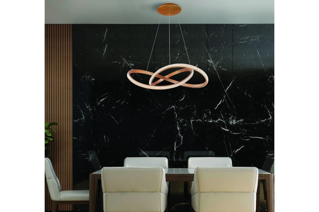 Lampa wisząca Infinity D80 w kolorze złotym z pilotem, składająca się z trzech okręgów w kształcie nieskończoności, zawieszona na cienkich linkach. Ujęcie z dołu, w tle czarna marmurowa ściana i białe krzesła obok drewnianego stołu.
