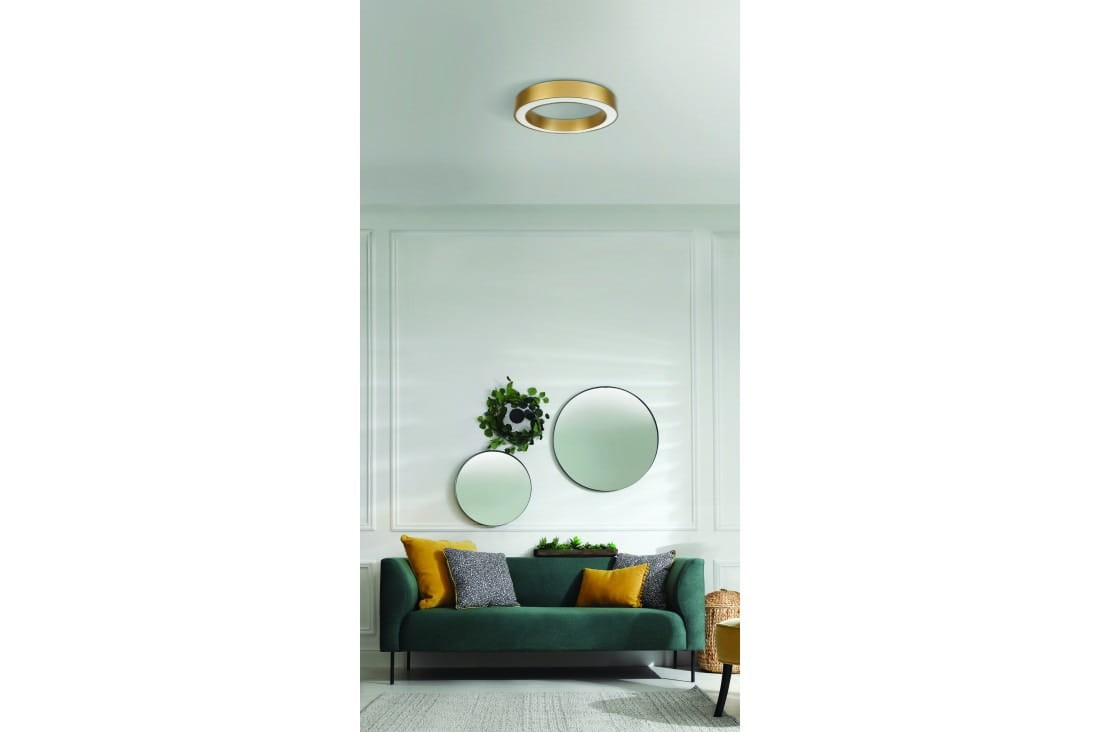 Plafon LED Marco D40 w kolorze złotym, o okrągłym kształcie, zamontowany na suficie. W tle widoczny zielony sofa z poduszkami w różnych kolorach oraz lustra w okrągłych ramach na ścianie.