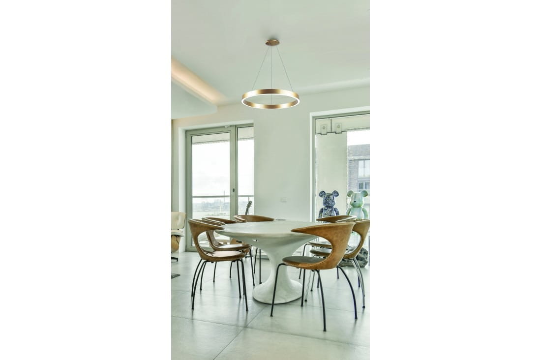 Lampa wisząca Marco D60 w kolorze złotym, z okrągłym kloszem, zawieszona nad okrągłym stołem. W tle widoczne okna oraz nowoczesne krzesła. Oświetlenie LED o regulowanej temperaturze barwowej 3000-6500K, sterowane pilotem.