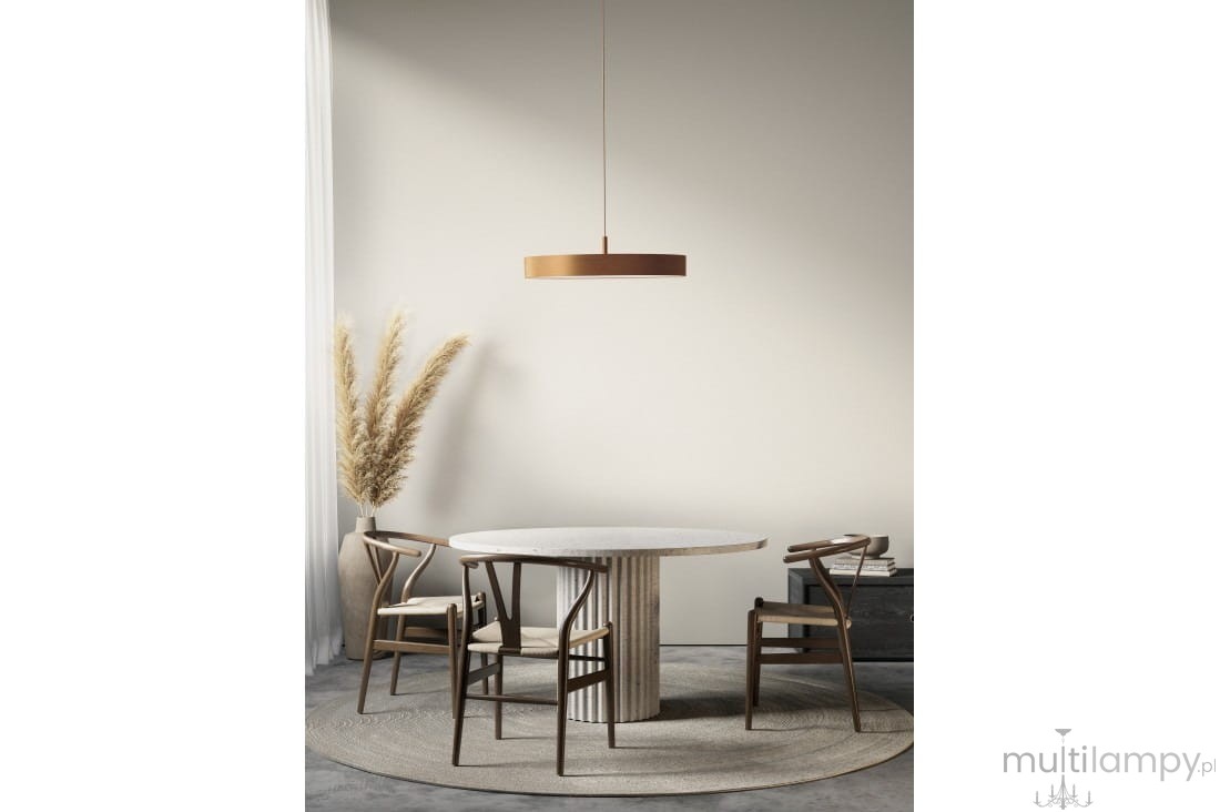 Złota lampa wisząca Marcello D60 z regulacją temperatury barwowej 3000-6500K, zawieszona nad okrągłym stołem. Widoczny minimalistyczny design oraz otoczenie z drewnianymi krzesłami i dekoracyjną roślinnością w tle.