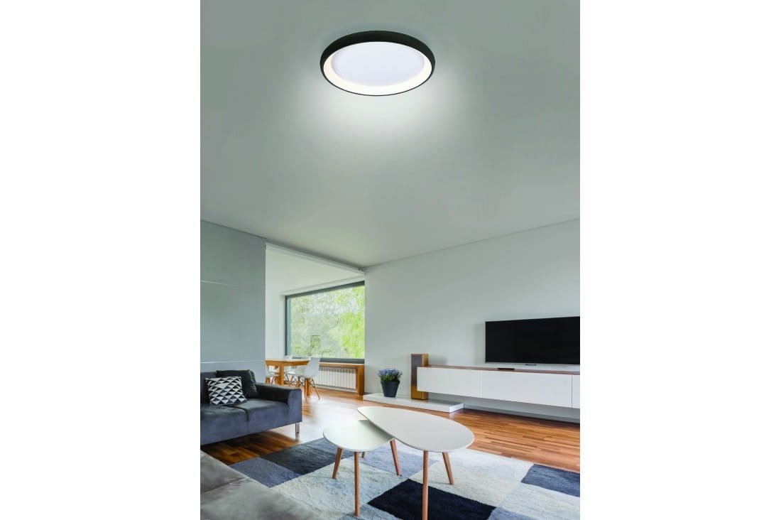 Czarny plafon LED Antonio D41, regulowany w zakresie 3000-6500K, zamontowany na suficie, okrągły kształt z białym kloszem. Widoczny w nowoczesnym wnętrzu z sofą, stolikiem kawowym oraz telewizorem. Pilot do zdalnego sterowania obok.