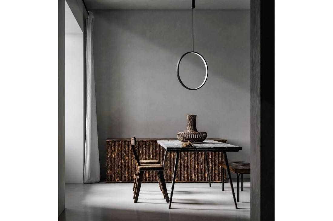 Czarna lampa wisząca Massima D40 LED w kształcie pierścienia, zawieszona nad stołem. Lampa ma minimalistyczny design, w otoczeniu drewnianych mebli i dekoracji, na tle szarej ściany.