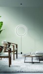 Czarna lampa wisząca Codutti LED 1-punktowa, w kształcie okręgu, zawieszona na cienkim przewodzie. W tle nowoczesny salon z drewnianymi krzesłami i okrągłym stolikiem na jasnym dywanie. Ściana w delikatnym odcieniu zieleni.