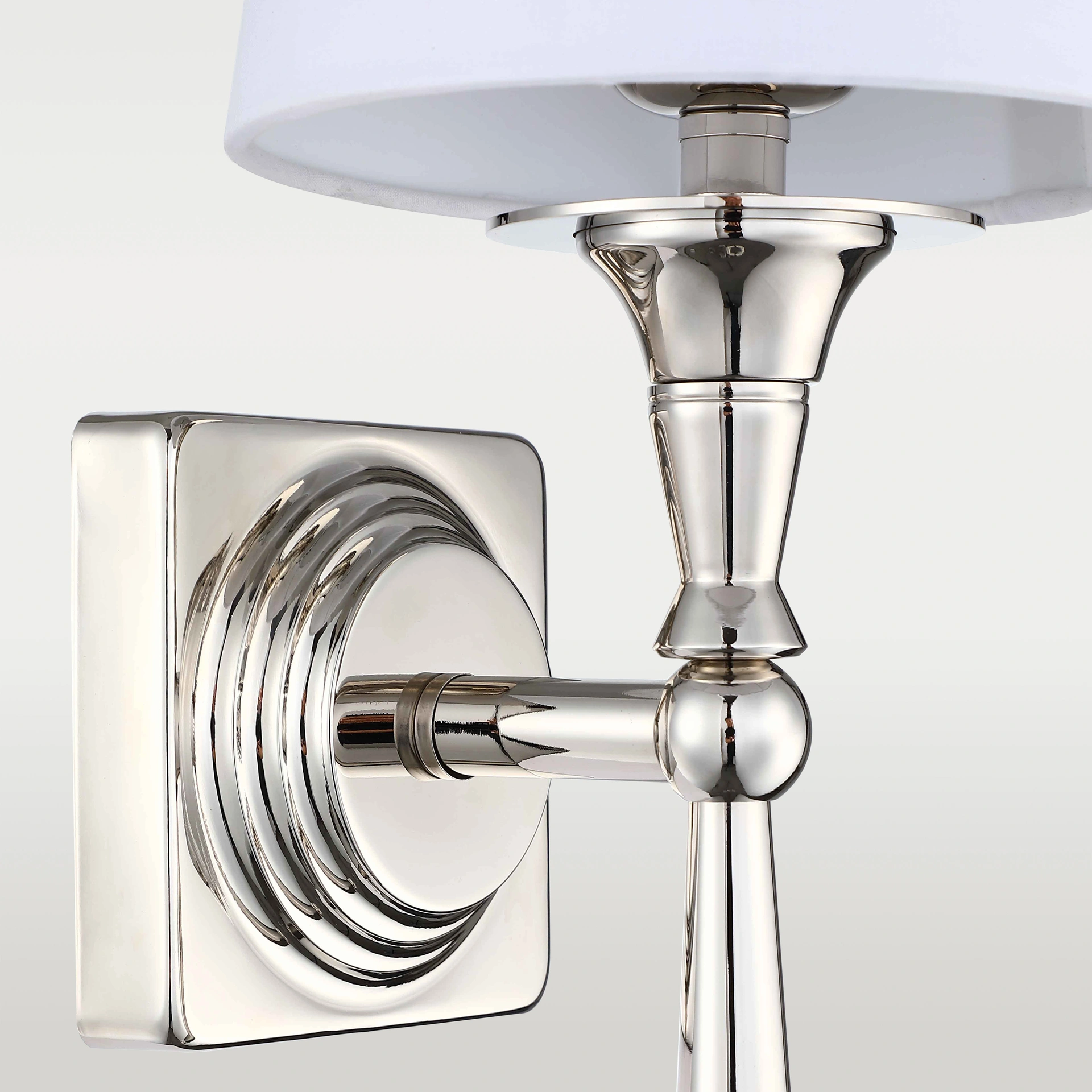 Kinkiet Austin 1-punktowy w kolorze niklowym z okrągłą, gładką podstawą oraz elegancką, stożkowatą oprawą. Lampa posiada biały abażur, montowana na ścianie, z wyraźnymi detalami i lśniącą powierzchnią.