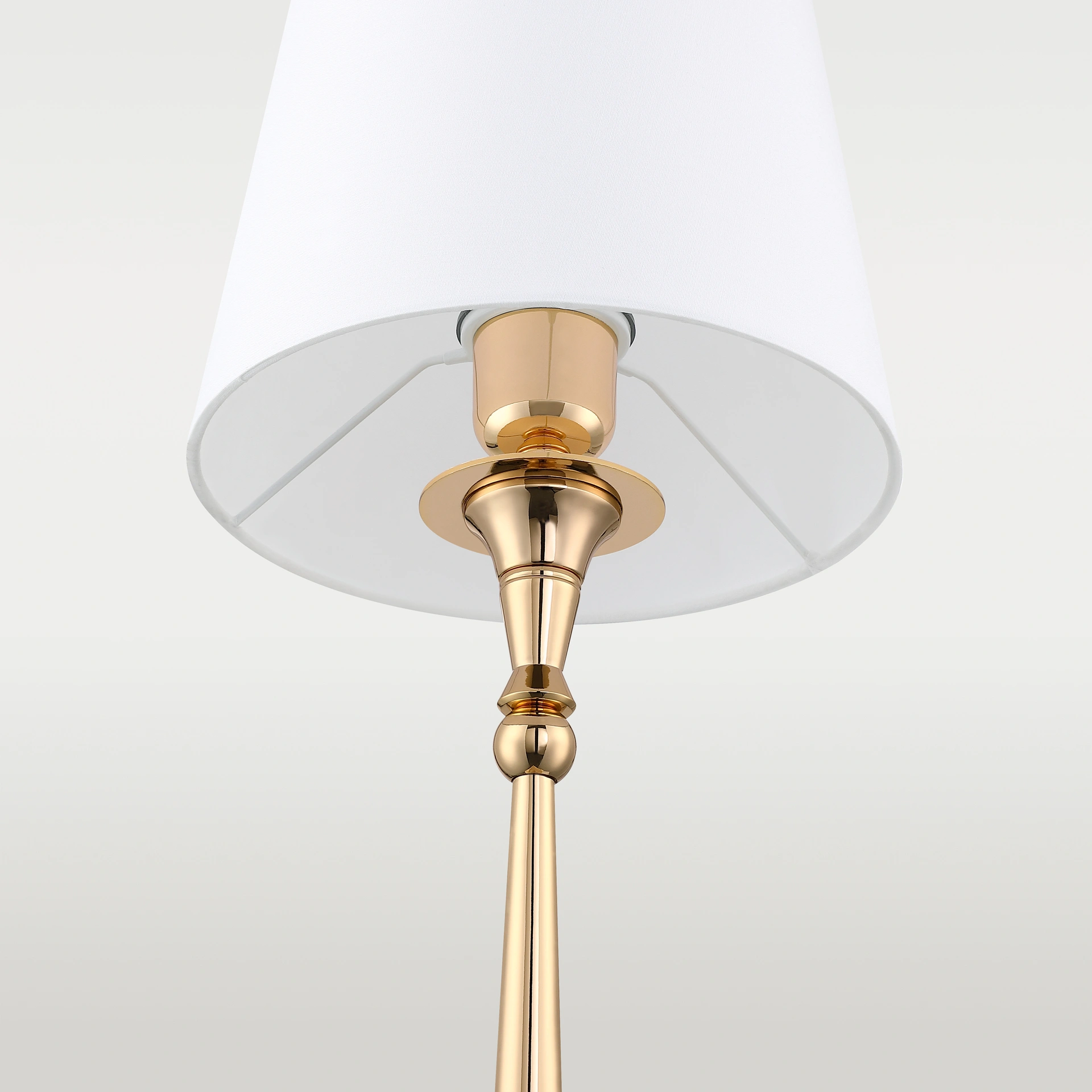 Lampa stołowa Austin z jedną żarówką, złota podstawa z połyskiem, z białym abażurem. Ujęcie z dołu, widoczny detal mocowania abażura oraz elegancka forma podstawy.