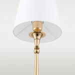 Lampa stołowa Austin z jedną żarówką, złota podstawa z połyskiem, z białym abażurem. Ujęcie z dołu, widoczny detal mocowania abażura oraz elegancka forma podstawy.
