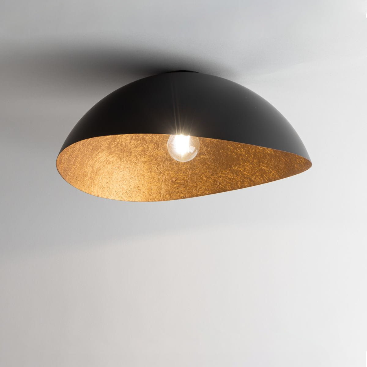 Lampa sufitowa Solaris M w kolorze czarnym z miedzianym wnętrzem, w kształcie półkuli, zamontowana na suficie. Widoczna żarówka w centralnej części, lampa emituje ciepłe światło. Tło jasne, minimalistyczne.