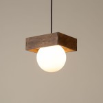 Czarna/brązowa lampa wisząca Bloom z okrągłym kloszem z białego szkła. Ujęcie z dołu, produkt zawieszony na czarnym przewodzie. Kwadratowa drewniana podstawa z widocznym usłojeniem, nadająca rustykalny charakter. Tło w jasnym odcieniu.