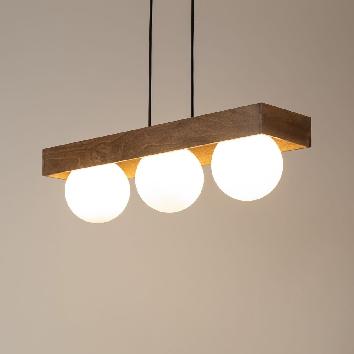 Lampa wisząca Bloom 3-punktowa w kolorze czarnym i brązowym, z drewnianym, prostokątnym podwieszeniem oraz trzema okrągłymi, białymi kloszami. Zawieszona na dwóch czarnych przewodach, prezentuje minimalistyczny design.