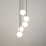 Lampa wisząca Piano 5-punktowa, czarna, z pięcioma okrągłymi, białymi kloszami zawieszonymi na czarnych przewodach. Klosze mają złote detale u podstawy, tworząc nowoczesny design. Lampa wisi w centralnej części zdjęcia na jasnym tle.