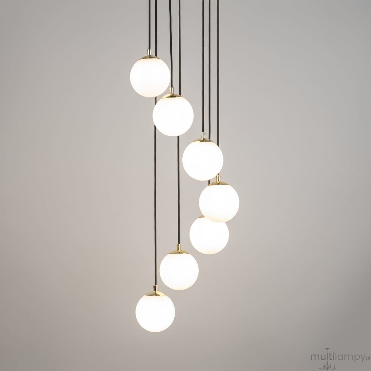 Czarna lampa wisząca Piano z siedmioma okrągłymi kloszami w białym kolorze, zawieszona na cienkich, czarnych przewodach. Klosze mają złote detale u góry, tworząc nowoczesny wygląd. Lampa jest zawieszona w pionie, na jednolitym, jasnoszarym tle.