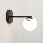 Kinkiet Piano 1-punktowy w kolorze czarnym z okrągłą, białą oprawą. Lampa przymocowana do ściany, z prostym metalowym ramieniem i złotym detalem przy źródle światła. Tło jasne, co podkreśla elegancki design.