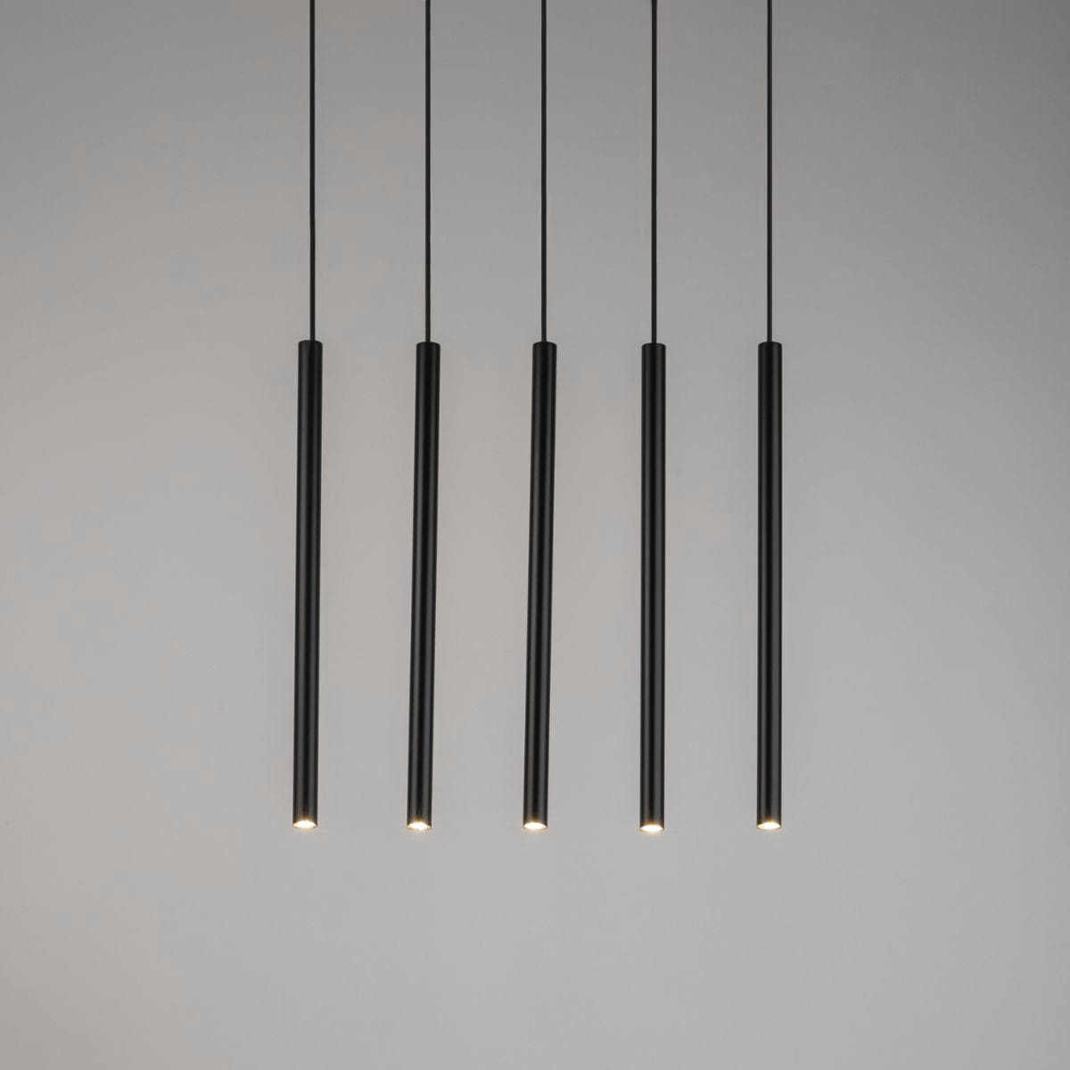Czarna, pięciopunktowa lampa wisząca Sopel Prosty, składająca się z pięciu wąskich, cylindrycznych elementów o matowej fakturze. Ujęcie z przodu, z lampą zawieszoną na cienkich linkach, na jasnym tle.