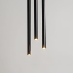 Czarna, wisząca lampa 3-punktowa Sopel Koło z trzema cylindrycznymi kloszami, emitującymi ciepłe światło. Lampa zawieszona w pionie, z minimalistycznym designem, na jasnym tle.