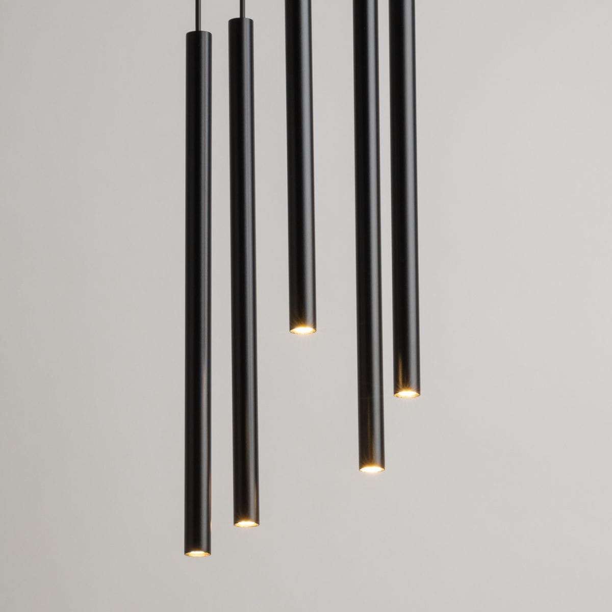 Lampa wisząca Sopel Koło w kolorze czarnym, składająca się z pięciu wydłużonych cylindrów. Ujęcie z góry, akcentujące źródła światła na końcach lamp. Prosty, nowoczesny design, zawieszona na cienkich linkach na jednolitym tle.