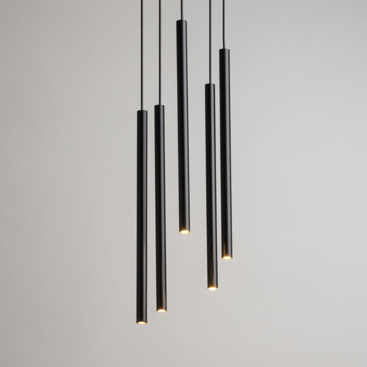 Lampa wisząca Sopel Koło, czarna, składająca się z pięciu długich cylindrycznych elementów. Źródła światła umieszczone na końcach, zawieszone na cienkich linkach. Prosty, nowoczesny design na jasnym tle.