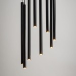 Lampa wisząca Sopel Koło, 8-punktowa, czarna. Składa się z ośmiu cylindrycznych elementów w różnych długościach, emitujących światło z końców. Zawieszona na cienkich linkach, w minimalistycznym stylu, na jasnym tle.