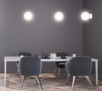 Biały kinkiet Rossi 1-punktowy z bursztynowym kloszem, zamontowany na szarej ścianie. Widoczny w nowoczesnej aranżacji jadalni z białym stołem i szarymi krzesłami. Klosz ma okrągły kształt, emitując ciepłe światło.