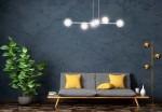 Lampa wisząca Rossi 6-punktowa w kolorze białym z mixem przezroczystych kul. Zawieszona nad szaro-beżową sofą z żółtymi poduszkami, w otoczeniu zielonej rośliny w donicy i złotej lampy stojącej. Tło w ciemnym odcieniu.