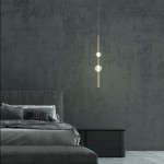 Lampa wisząca Vaku w kolorze złotym z dwoma kulistymi źródłami światła LED, zawieszona nad łóżkiem w sypialni. Prosta, elegancka forma z metalowym stelażem. Tło w ciemnym odcieniu, co podkreśla design.