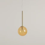 Lampa wisząca Bosso D14 z mosiężnym uchwytem i okrągłym kloszem w kolorze pomarańczowym. Ujęcie z przodu, zawieszona na cienkim przewodzie. Przeznaczona do jednej żarówki G9. Tło jasne i jednolite.