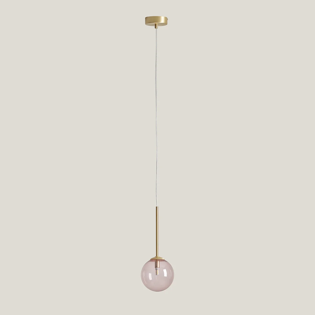 Lampa wisząca Bosso D14 z mosiężnym uchwytem i różową, szklaną kulą. Produkt zawieszony na białym przewodzie, z okrągłym mosiężnym mocowaniem sufitowym. Idealna do nowoczesnych wnętrz.