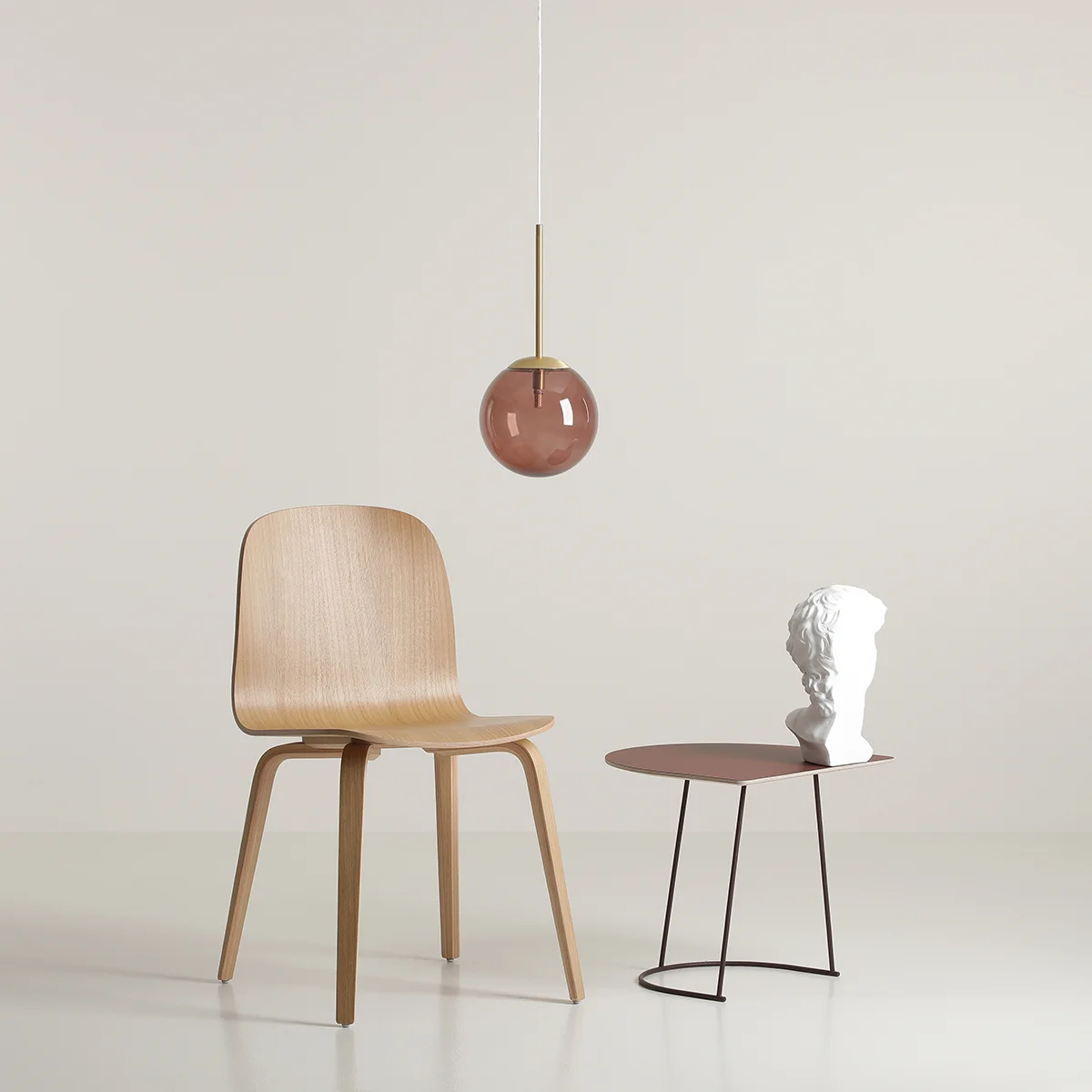 Lampa wisząca Bosso D14 w kolorze mosiądzu i choco cream z okrągłym, szklanym kloszem w odcieniu różowym. Umieszczona nad drewnianym krzesłem i stołem z metalowymi nogami, tworzy nowoczesną aranżację.