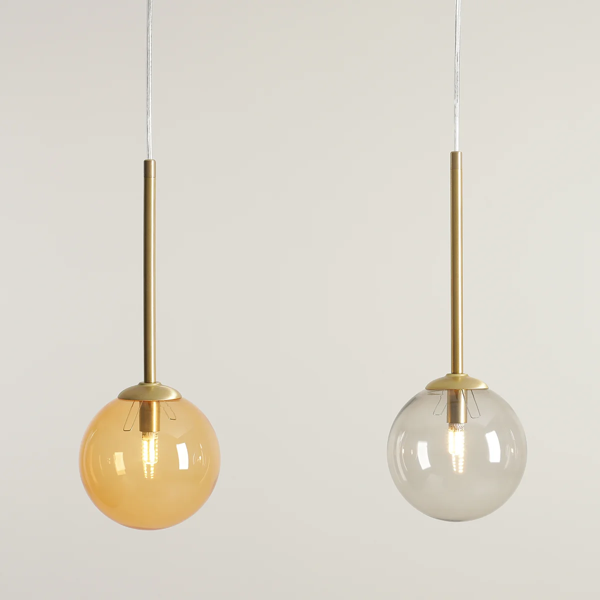 Lampa wisząca Bosso 3xG9 w kolorze mosiądzu z dwiema kulistymi kloszami: jeden przezroczysty, drugi w odcieniu bursztynu. Ujęcie z przodu, zawieszona na cienkim, białym przewodzie, z widocznym źródłem światła wewnątrz.