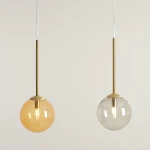 Lampa wisząca Bosso 3xG9 w kolorze mosiądzu z dwiema kulistymi kloszami: jeden przezroczysty, drugi w odcieniu bursztynu. Ujęcie z przodu, zawieszona na cienkim, białym przewodzie, z widocznym źródłem światła wewnątrz.