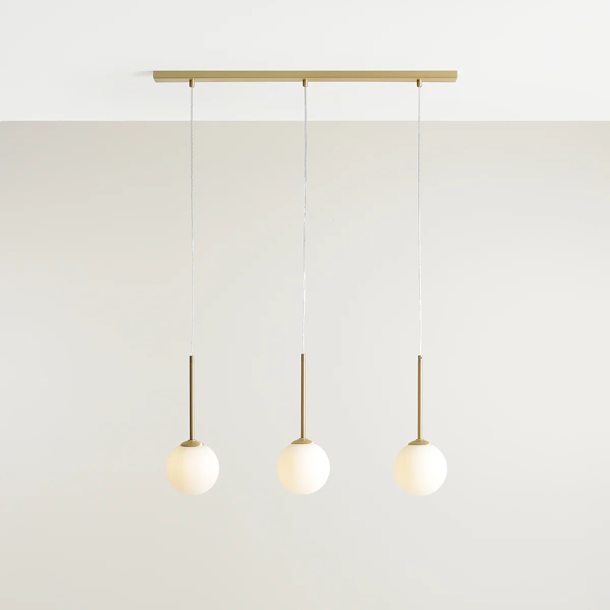 Lampa wisząca Bosso z trzema kulistymi kloszami w kolorze białym, zawieszona na mosiężnej konstrukcji. Klosze umieszczone na długich, smukłych rurkach, w prostym, nowoczesnym designie, zawieszone na cienkich linkach.
