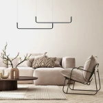 Czarna lampa wisząca Malawi LP-1015/2P z dwoma źródłami LED, umieszczona nad jasną sofą w nowoczesnym wnętrzu. Prosty, geometryczny kształt. W tle widoczna dekoracyjna gałązka z kwiatami i stół kawowy.