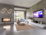 Kinkiet LED Wand 466 o mocy 6W w kolorze białym i złotym, zamontowany na betonowej ścianie. Wyposażony w minimalistyczny design, emituje ciepłe światło, dopełniając nowoczesne wnętrze. W tle widoczny kominek i telewizor.