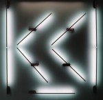 Kinkiet LED Line 243A o mocy 10W w kolorze czarnym. Produkt montowany na ścianie, składający się z ukośnych linii świetlnych, emitujących delikatne światło. Widoczne mocowania w formie prostokątnych uchwytów. Tło jasne, co podkreśla efekt świetlny.