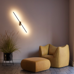 Kinkiet LED Line 243A, czarny, o mocy 10W, zamontowany na ścianie pod kątem, emitujący ciepłe światło. W tle widoczny żółty fotel i pufa, a także donica z trawą, tworząc przytulną aranżację wnętrza.