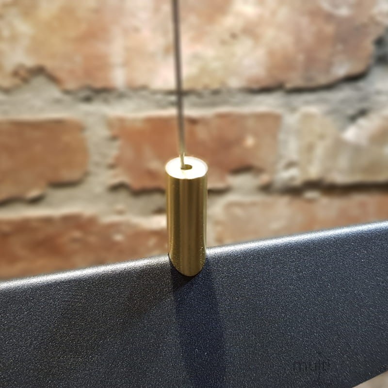 Czarna lampa wisząca LED Buket 357 z metalowym złotym detalem. Widok na złoty element mocujący oraz górną część lampy na tle ceglanej ściany. Lampa ma nowoczesny design z prostą, matową powierzchnią.
