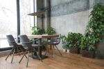 Lampa wisząca LED Buket 357 w kolorze czarnym i złotym, zawieszona w pomieszczeniu, nad drewnianym stołem. Widoczne metalowe detale i geometryczny kształt. W tle roślinność w doniczkach oraz nowoczesne krzesła.