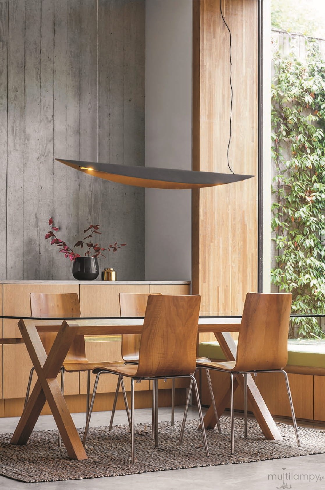Lampa wisząca LED Buket 357, czarna z złotym akcentem, o nowoczesnym, smukłym kształcie. Zawieszona nad drewnianym stołem w jadalni, z otoczeniem w neutralnych barwach. Widoczny sznurek mocujący oraz detale lampy, emitująca ciepłe światło.
