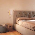 Kinkiet Hotels 417H w kolorze białym, montowany na ścianie, z podwójnym oświetleniem LED 7W, portem USB oraz ładowarką indukcyjną. Widoczny na tle łóżka z tapicerowanym zagłówkiem w sypialni.